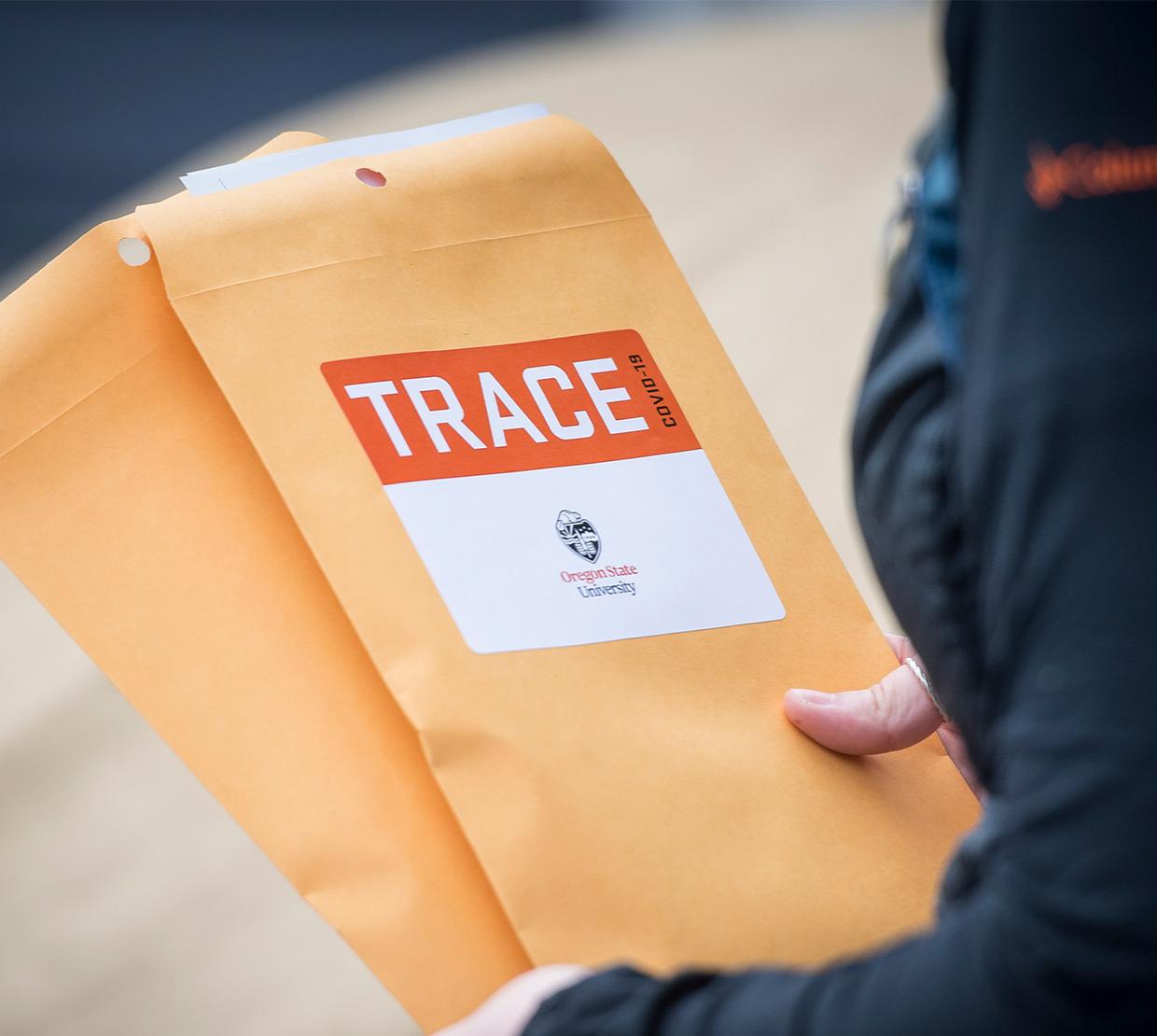 TRACE field staff member holding manilla envelopes with TRACE stickers on them.