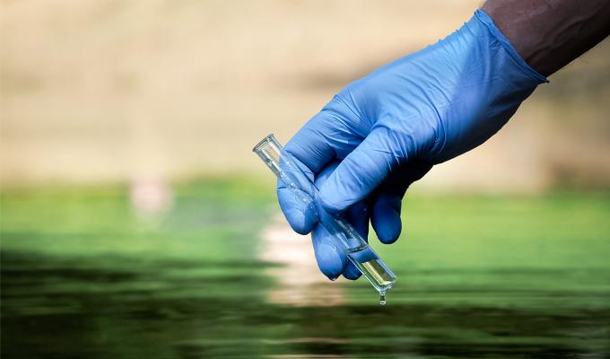 Gloved hand holding water test tube above wastewater.